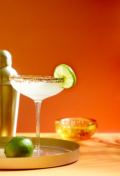 Cocktail with lime garnish on an orange background