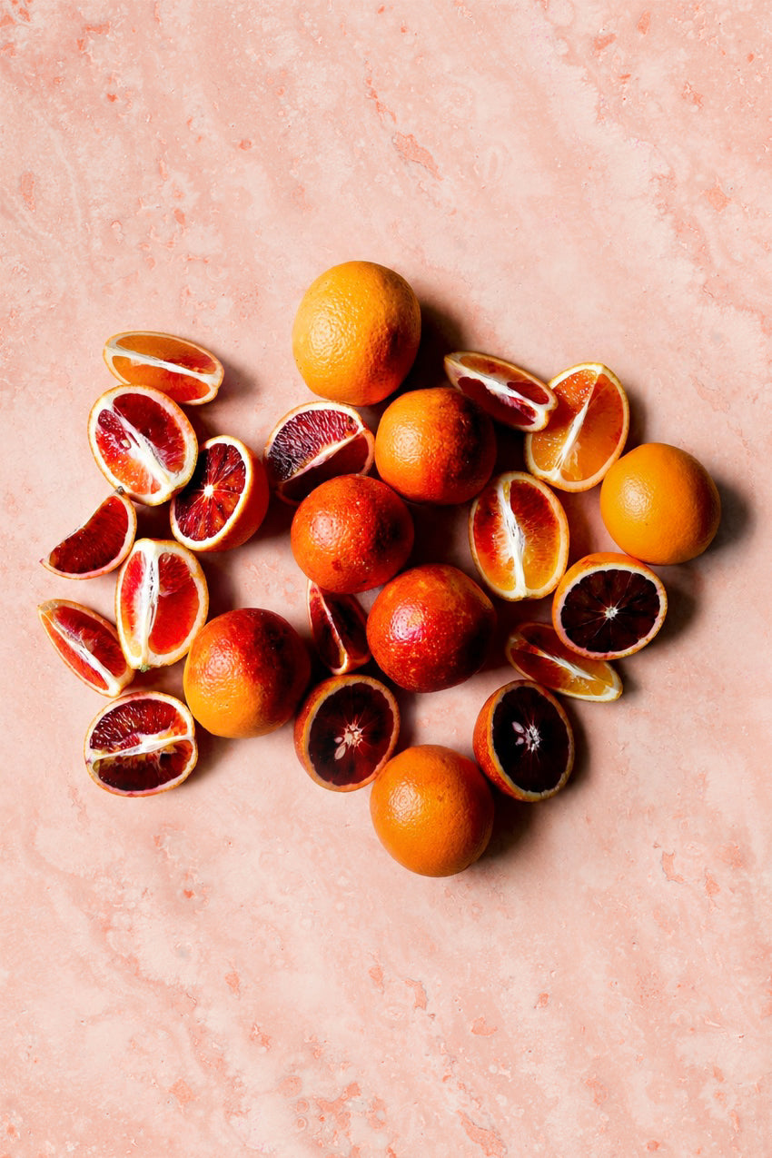 Sliced blood oranges on a pink swirling marble-effect vinyl photography backdrop.
