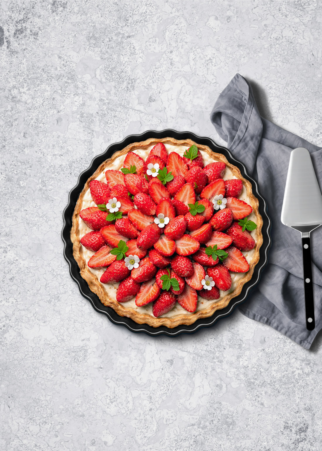 Styled strawberry tart on a grey photography surface with a knife and napkin.