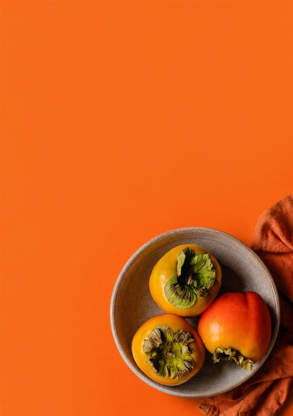 Three persimmons in a bowl on an orange background