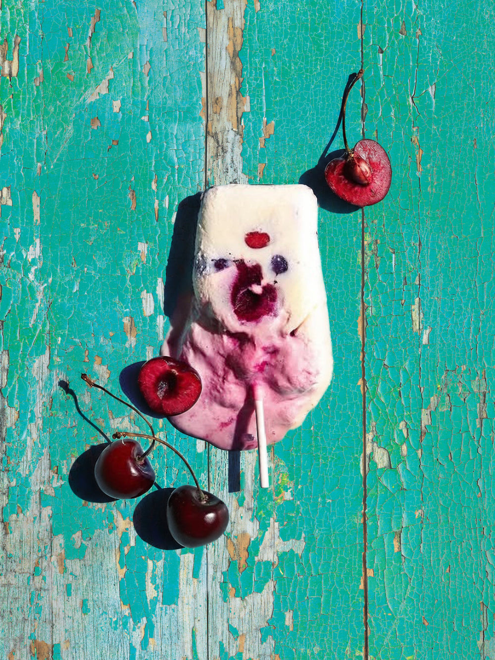Flat lay of a melting icecream with fresh red cherries on a distressed turquoise and green coloured flaky wood effect vinyl photography backdrop.