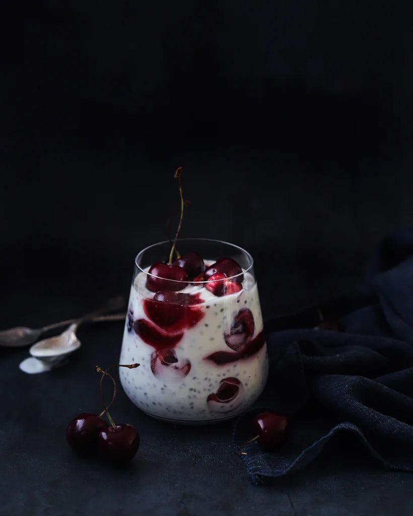 Glass of dessert with cherries styled on a vinyl photography backdrop showing a subtle, deep steely blue grey colour.