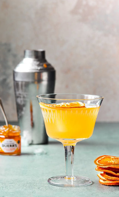 Orange cocktail in a glass with a shaker and orange slices on a light background