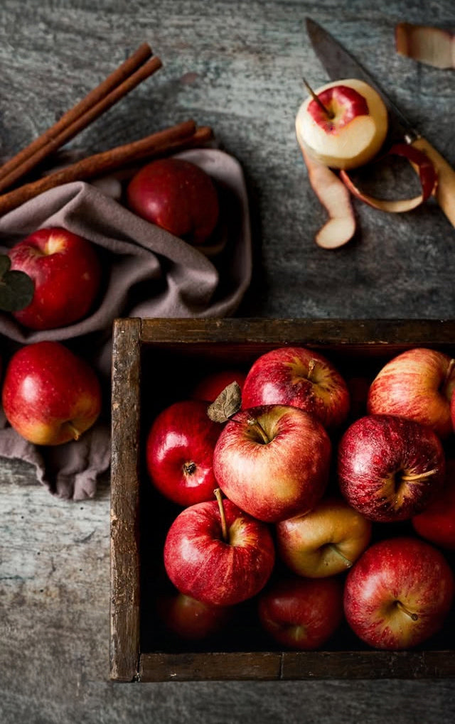 Apples in a wooden crate with cinnamon sticks on a rustic photography backdrop