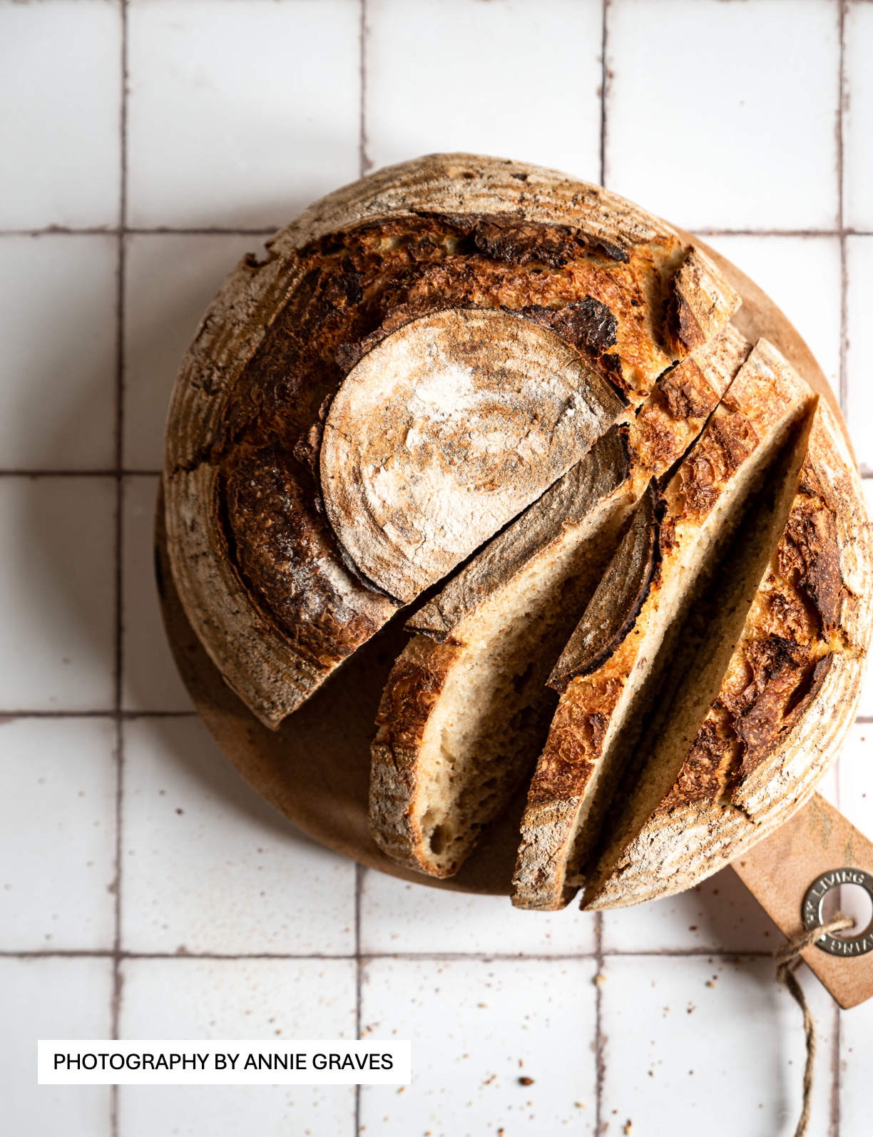 Rustic farmhouse bread styled on a white tile effect photography backdrop with a subtle gray grid lines texture.