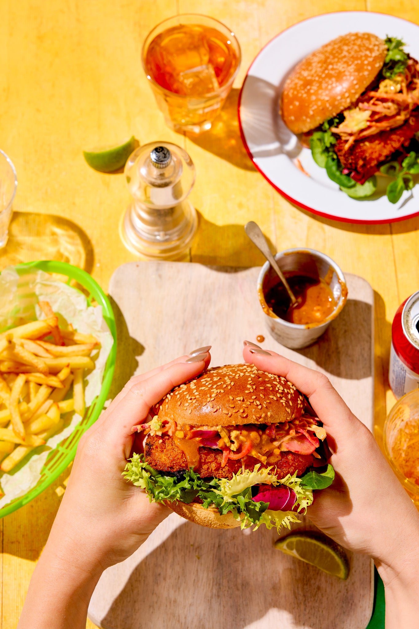 Brighly lit styled burger table scene shot on a saffron yellow wood-effect vinyl photography backdrop with visible wood grain.