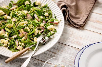 Close-up image of a green salad styled on a white and grey wood plank effect photography backdrop.