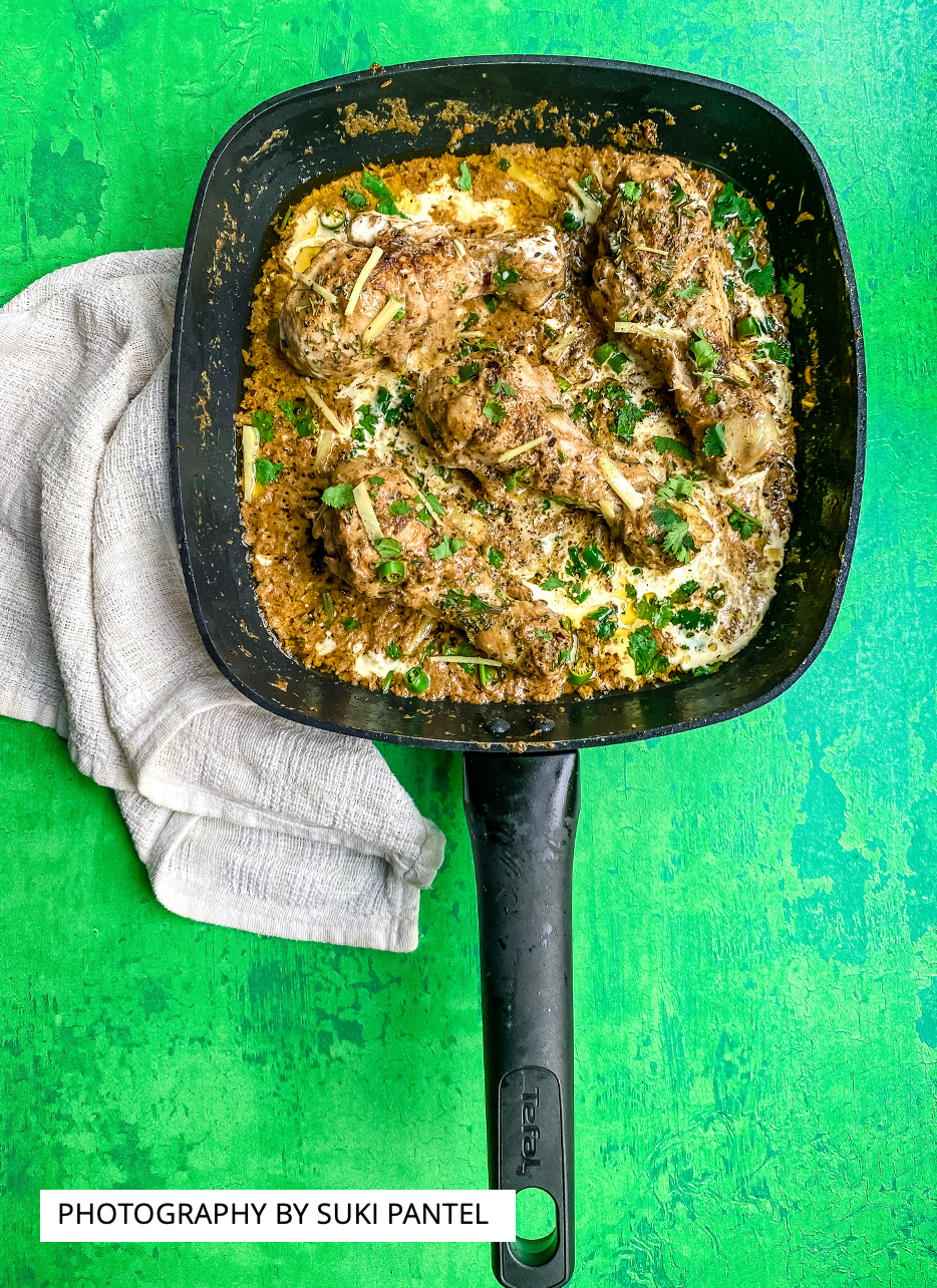 A flat lay of a pan of chicken korma curry styled on a vibrant green vinyl photography backdrop with a hand-painted effect.