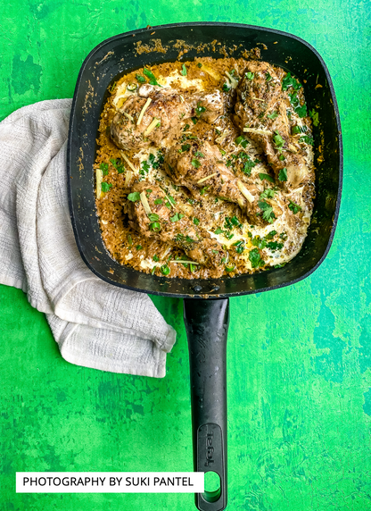 A flat lay of a pan of chicken korma curry styled on a vibrant green vinyl photography backdrop with a hand-painted effect.