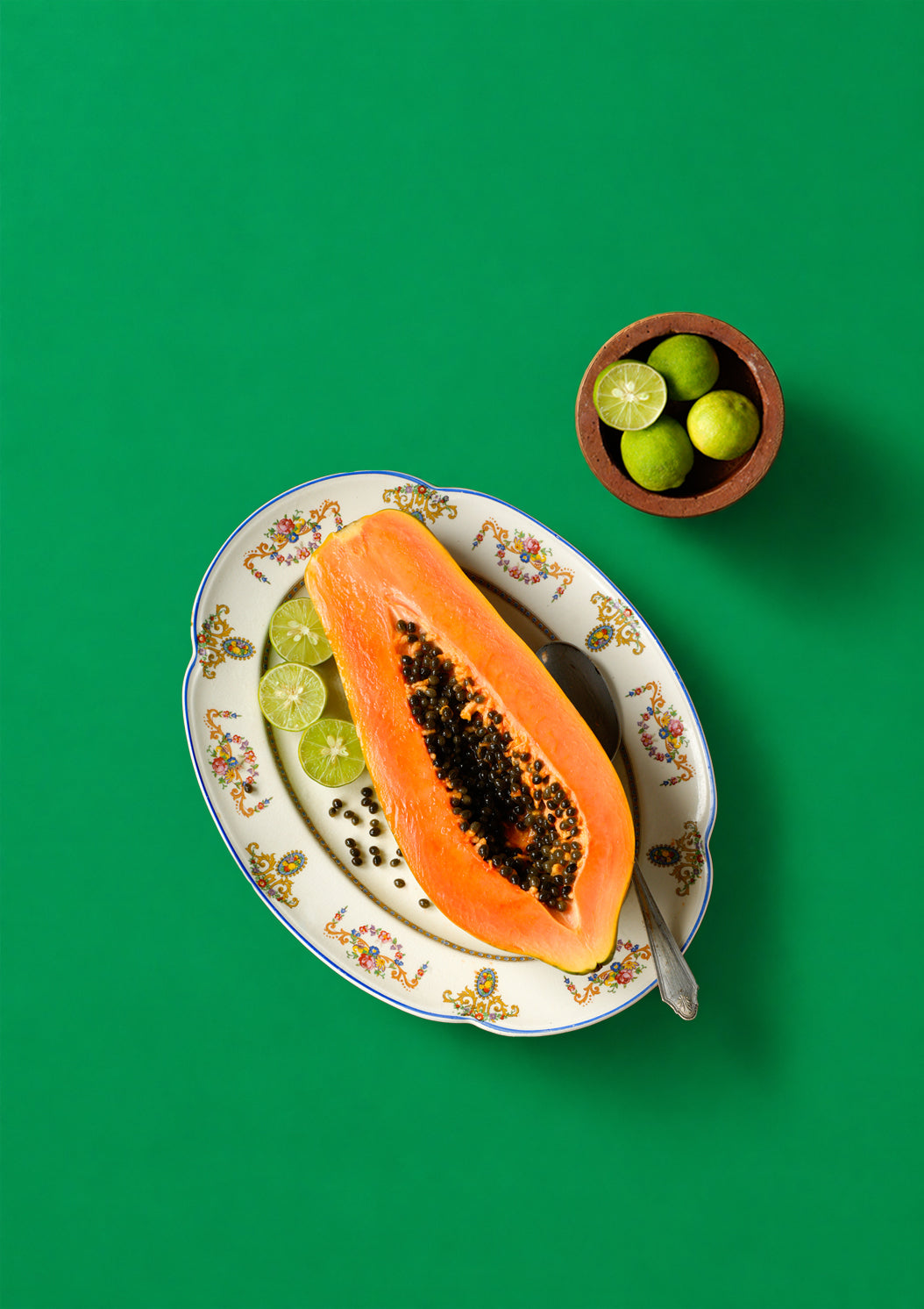 Sliced papaya on a decorative plate with limes on a green background