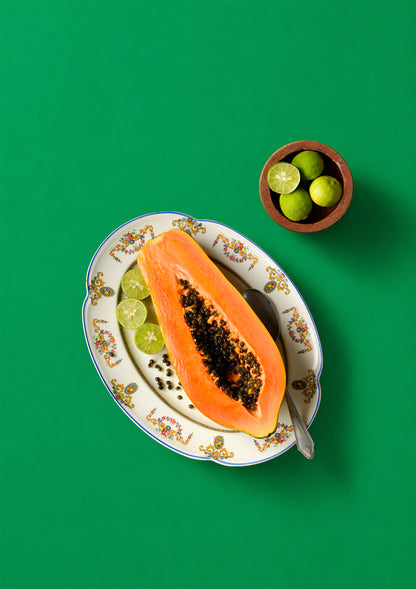 Sliced papaya on a decorative plate with limes on a green background