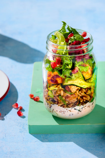 A jam jar filled with colourful pomegranate salad on a blue backdrop