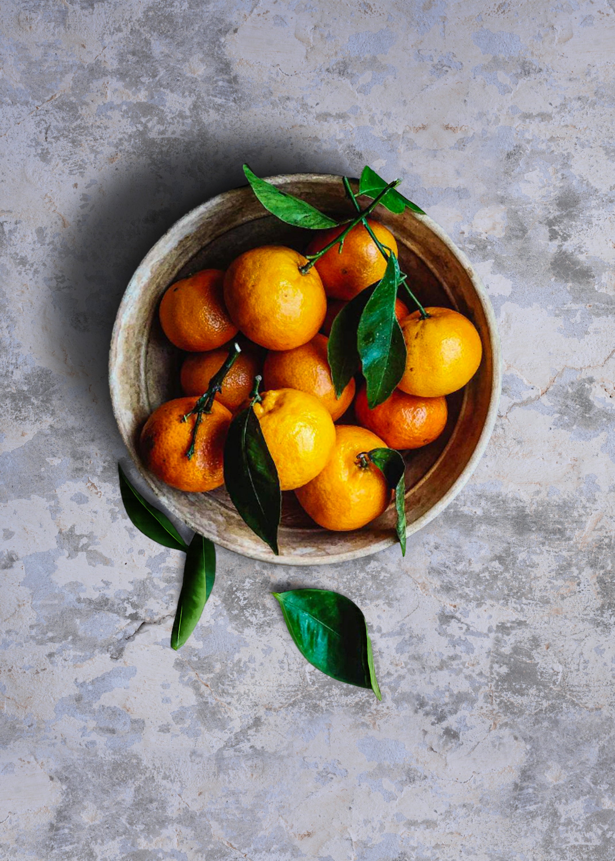 Bowl of oranges with leaves on a cool grey textured stone effect vinyl photography backdrop.