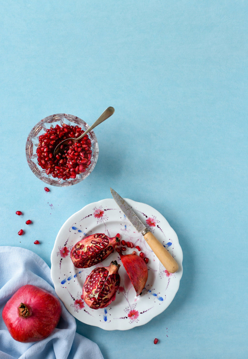 Flat lay of fresh pomegranates with vintage props styled on a pale blue plaster-effect vinyl photography backdrop ideal for food styling or as a beauty product photography background