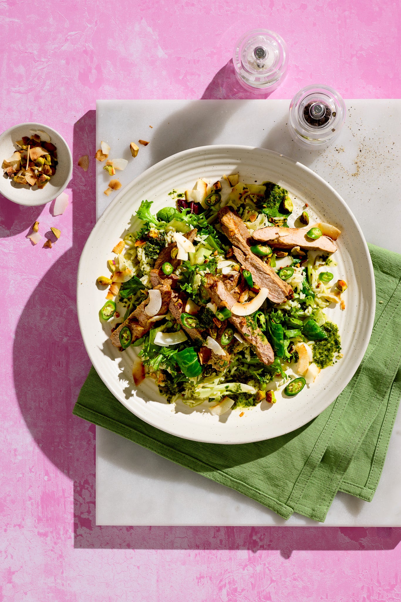 Flat lay of a salad and green napkin styled on a pink vinyl photography backdrop with an old weathered chalky paint effect texture.