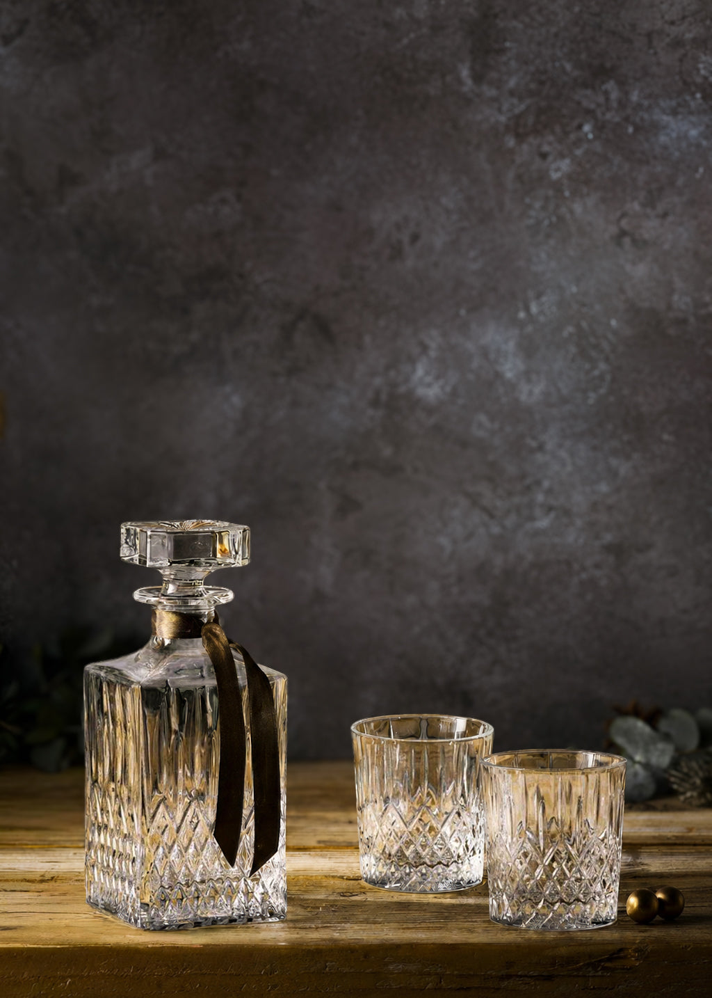 Crystal decanter and glasses on a wooden surface shot against a hand-painted mottled effect vinyl photography backdrop in mixed dark greys.