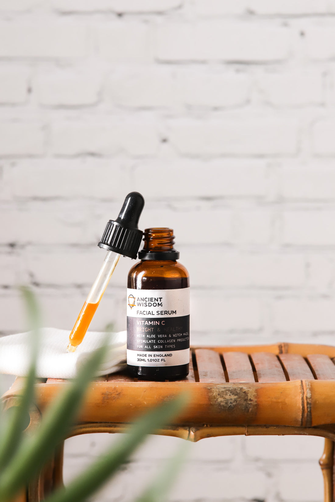 A facial serum against a white brick wall-effect vinyl photography backdrop with varying shades of grey and mortar lines designed to mimic a brick wall texture.