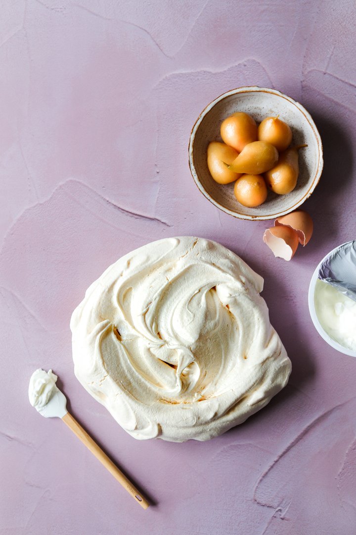 Top down shot of a meringue and poached pears in a bowl styled on a hand-trowelled soft blush pink plaster effect vinyl photography backdrop for food, jewellery and still life photography.
