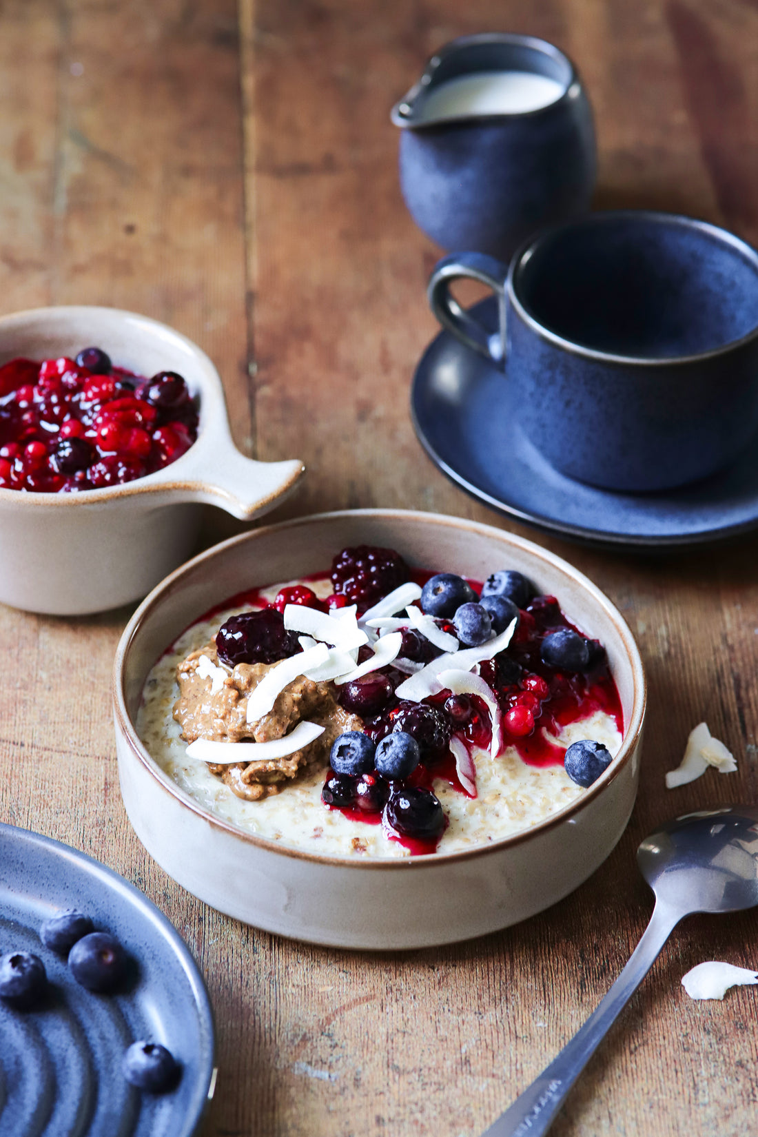 A styled image of a blue ceramic breakfast set with berry porridge on a wood-effect vinyl photography backdrop with natural color tones and visible grain details.