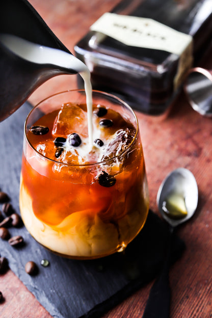 A styled image of a cold brew coffee in a glass on a wood-effect vinyl photography backdrop with natural color tones and visible grain details.