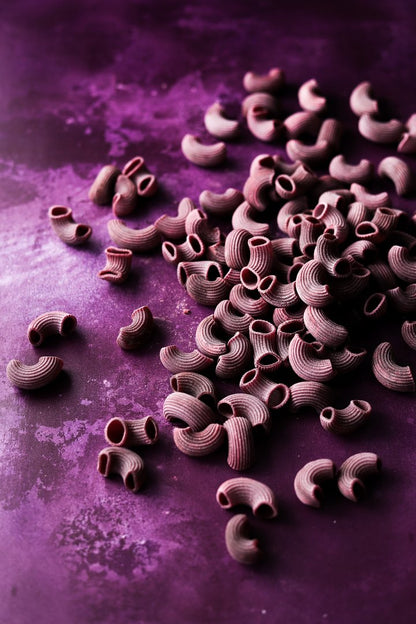 A pinky-purple food photography backdrop with a hand-painted effect, styled with handmade purple pasta shapes.