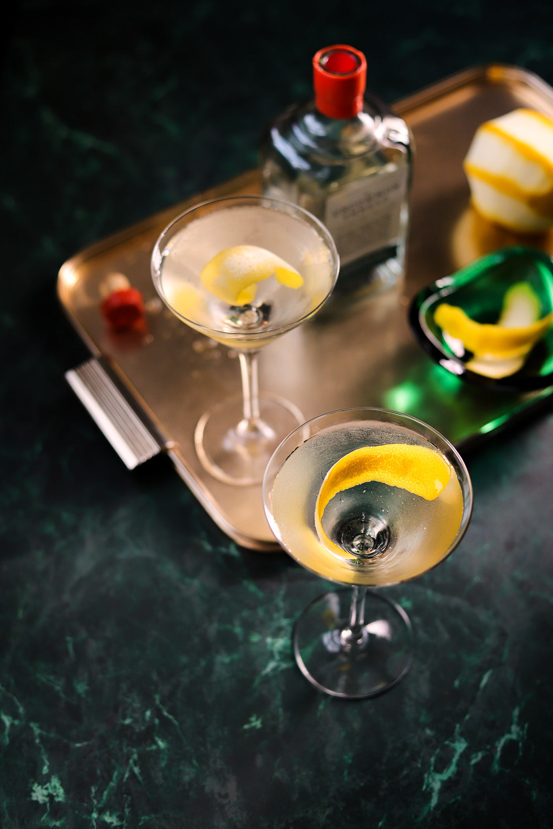 Gold tray of glamorous gin cocktails styled on a green marble effect vinyl photography backdrop.