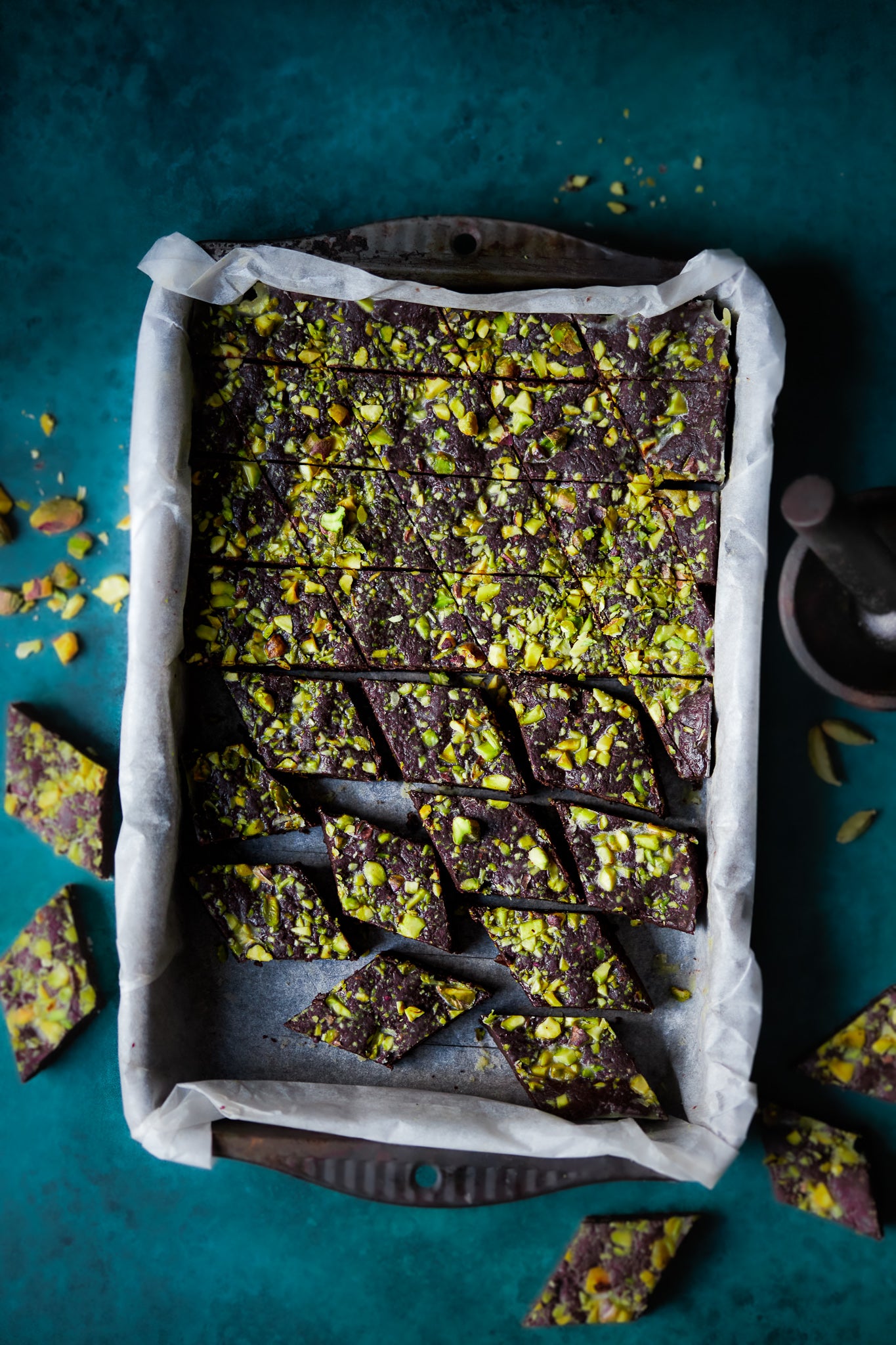 Chocolate and Pistachio baked brownie styled on a dark green, textured photography backdrop with a soft mottled effect 