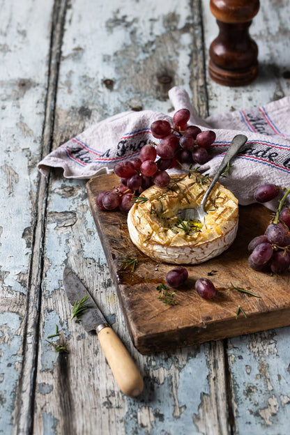 Old vintage flakey wood effect photography backdrop with a wooden board of Camembert cheese and grapes.
