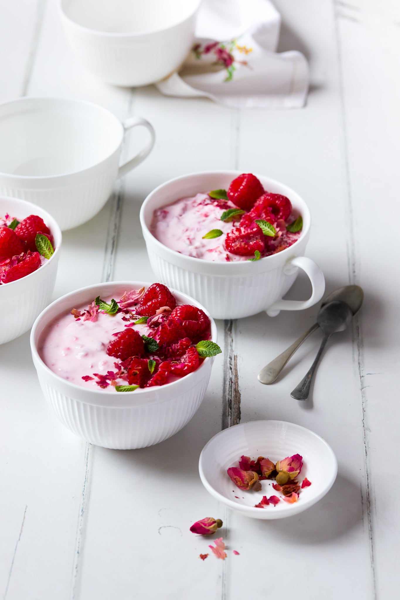 White mugs of raspberry food styling against a white painted wood photography backdrop with vertical planks displaying natural wear and tear beneath the paint.