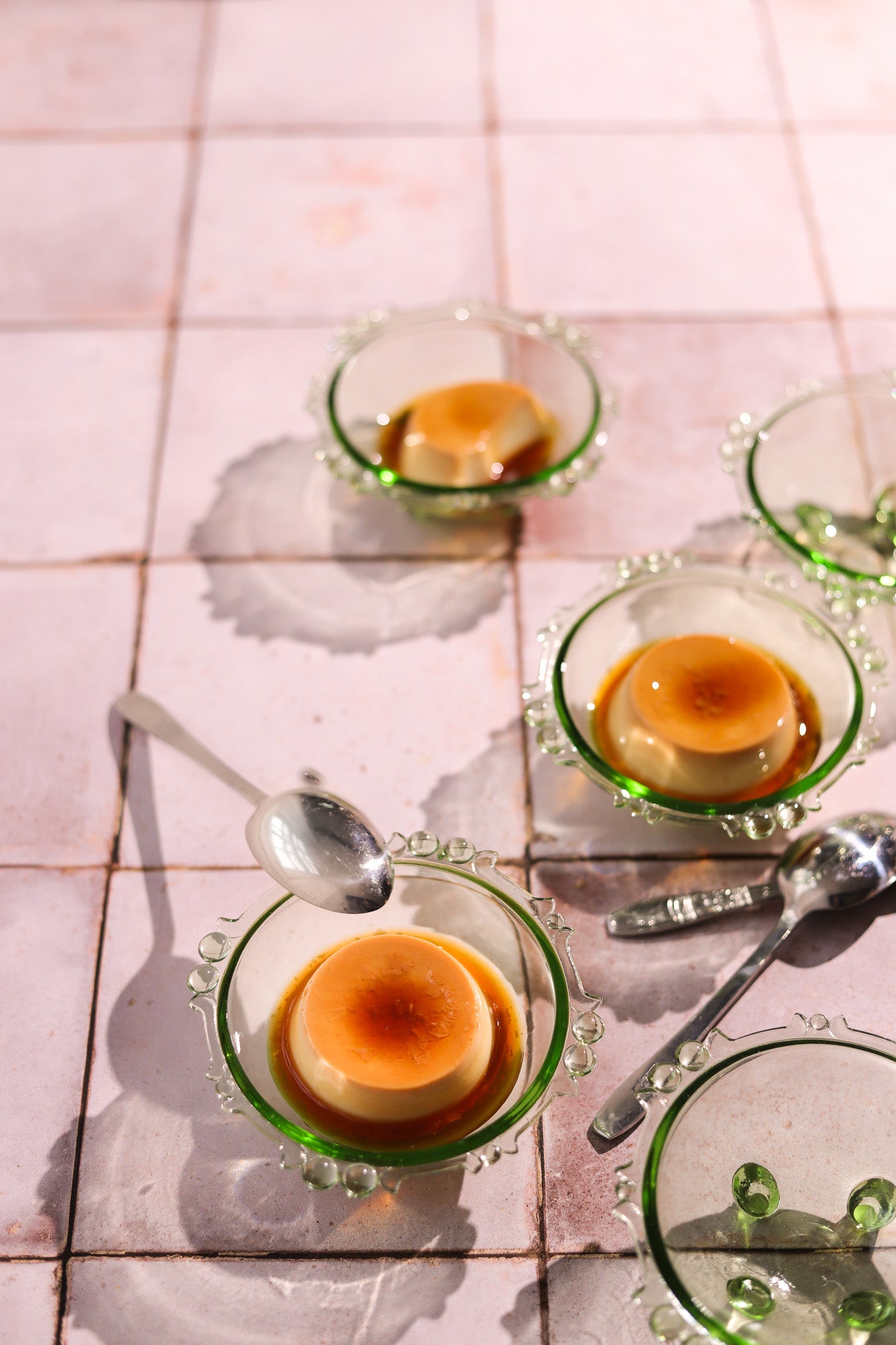 Crème Brûlée styled in green glasses dishes styled on a pink tile-effect vinyl photography backdrop with a vintage chalky tile effect.