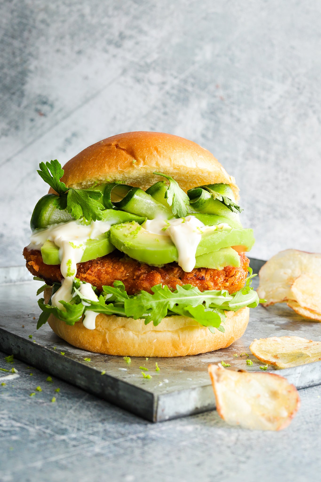 A fresh chicken burger styled against a weathered blue and grey effect hand painted photography backdrop, with a variety of greys and blues creating a textured appearance.