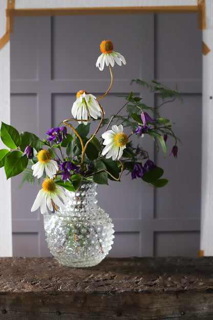 Glass vase and flowers against a taped panelled wall effect photography backdrop in warm grey with light and shadow details.