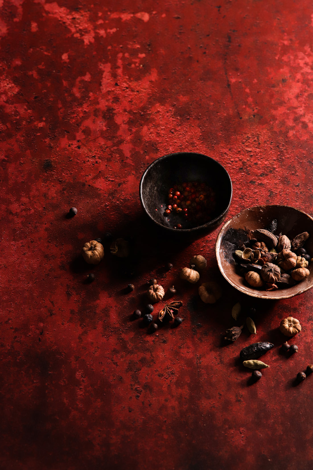 Flat lay shot of two small rustic bowls of nuts styled on a highly textured rusty red metal effect photography backdrop used for food and product styling.