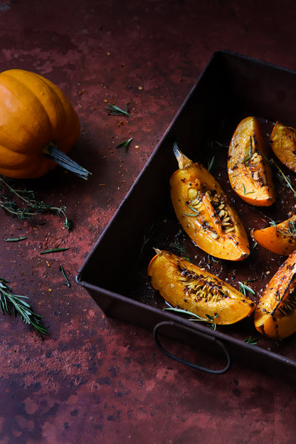 Flat lay shot of a tray of roasted pumpkins styled on a highly textured rusty red metal effect photography backdrop used for food and product styling.
