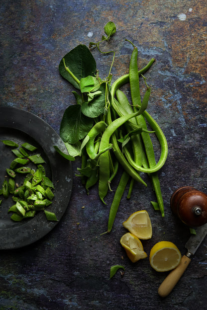 A flat lay image of fresh green beans styled on a brown textured slate-effect vinyl food photography backdrop.