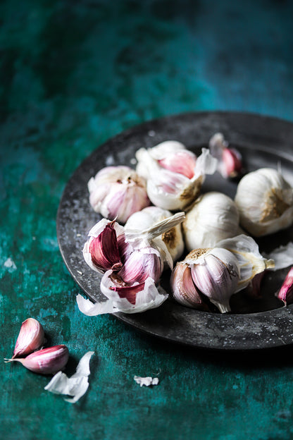 A vintage plate of fresh garlic bulbs styled on a vibrant green vinyl photography backdrop with flaky paint-effect texture.