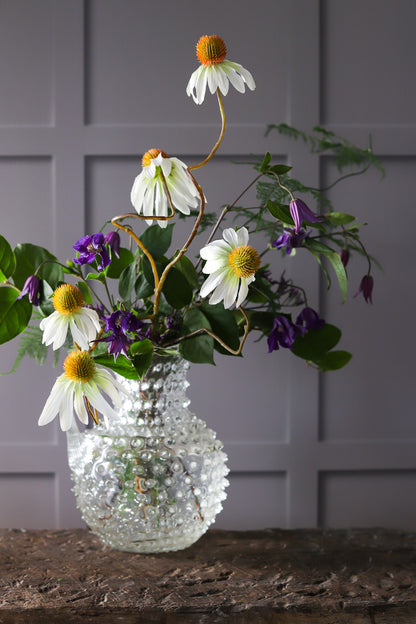Glass vase and flowers against a panelled wall effect photography backdrop in warm grey with light and shadow details.