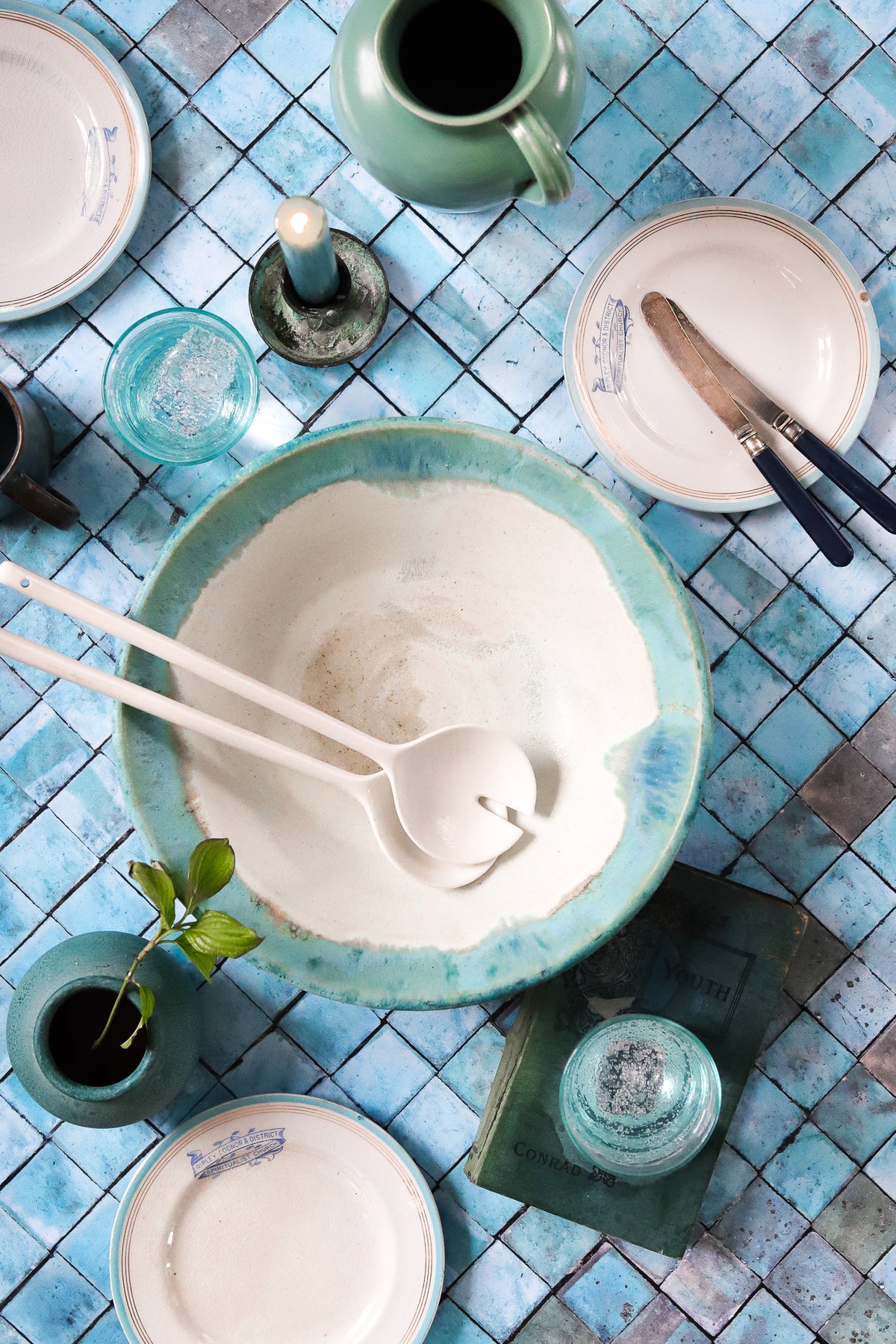 A flat lay of ceramics and tableware styled on a blue mosaic tile effect vinyl photography backdrop.