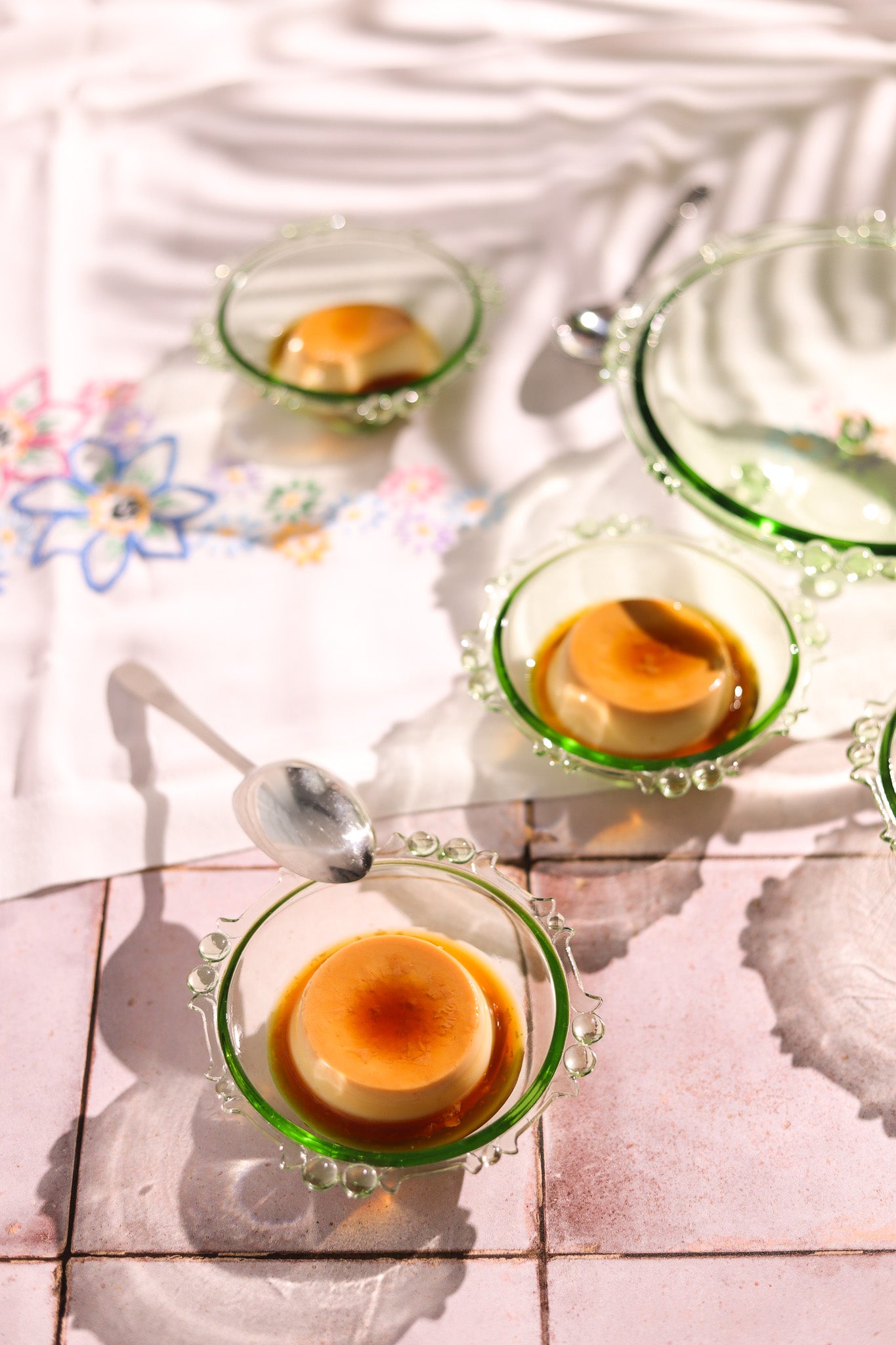 Crème Brûlée styled in green glasses dishes styled on a pink tile-effect vinyl photography backdrop with a vintage chalky tile effect.