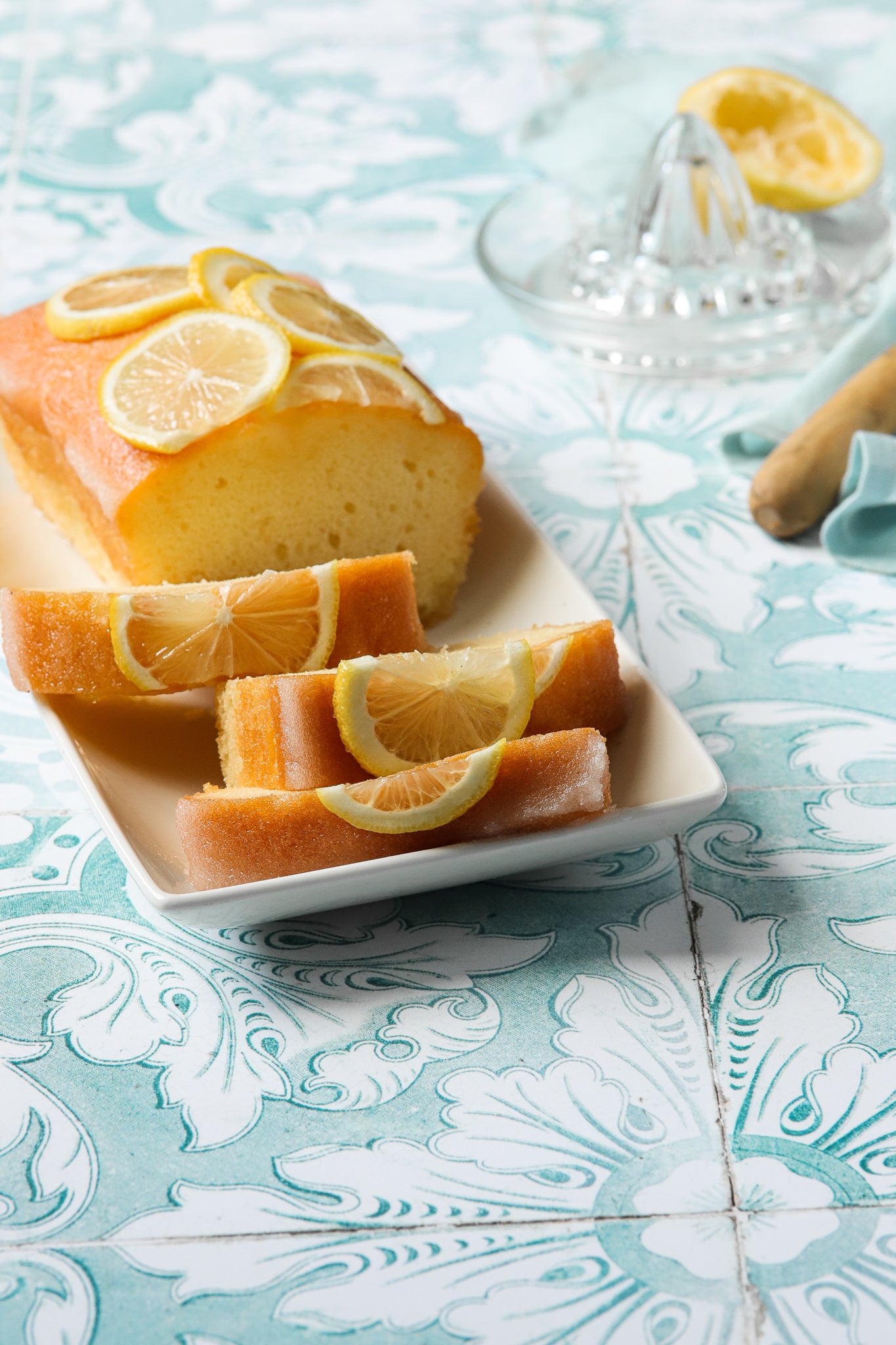 A sliced lemon cake styled on a soft jade green photography backdrop with a vintage Spanish tile pattern.