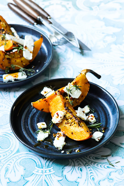 A blue ceramic plate of roasted butternut squash styled on a soft jade green photography backdrop with a vintage Spanish tile pattern.