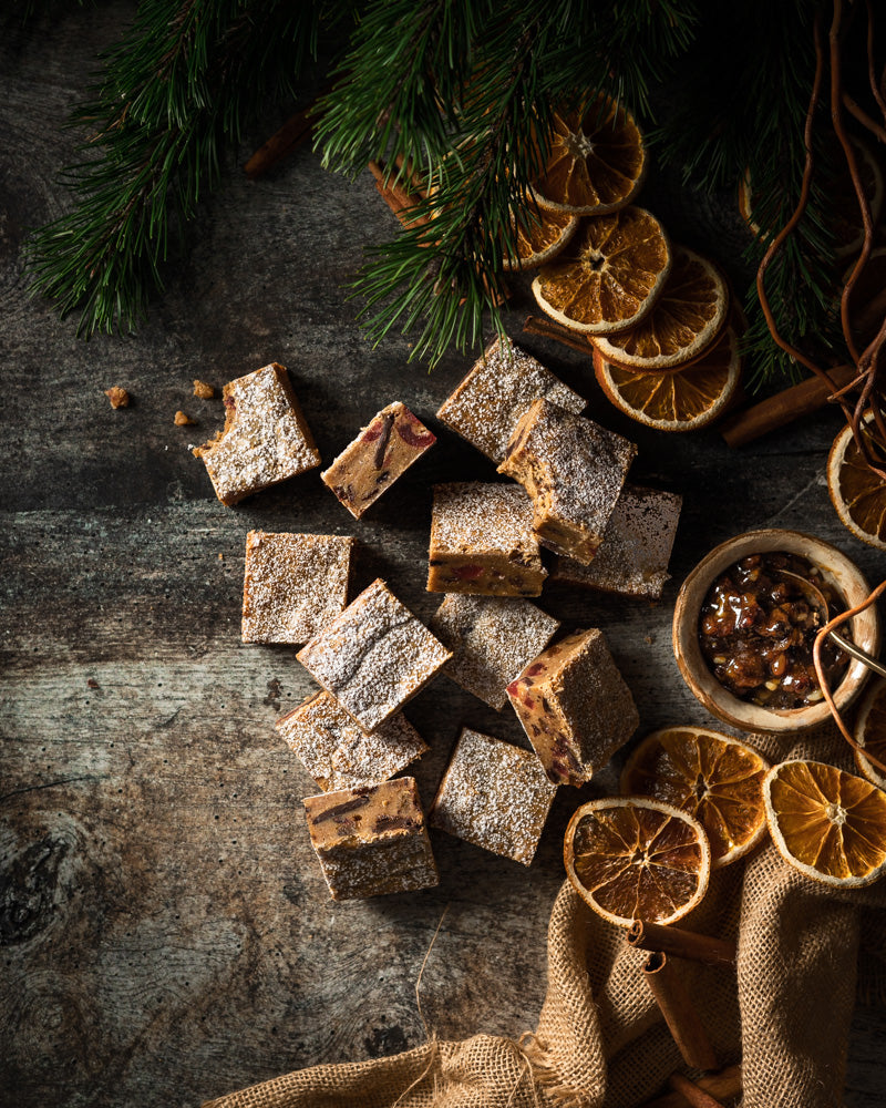 Christmas flat lay of dried orange slices, fir and homemade sweets styled on a rustic photography backdrop with an old wood brown and grey colour palette, suitable for food and product styling.