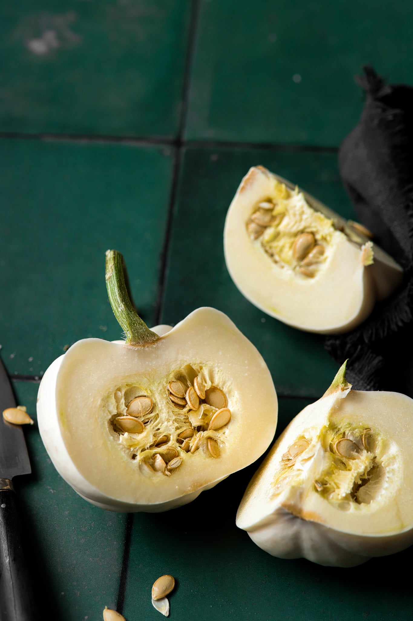 A styled image of freshly cut white squash on a green tile effect photography backdrop with an irregular patina.