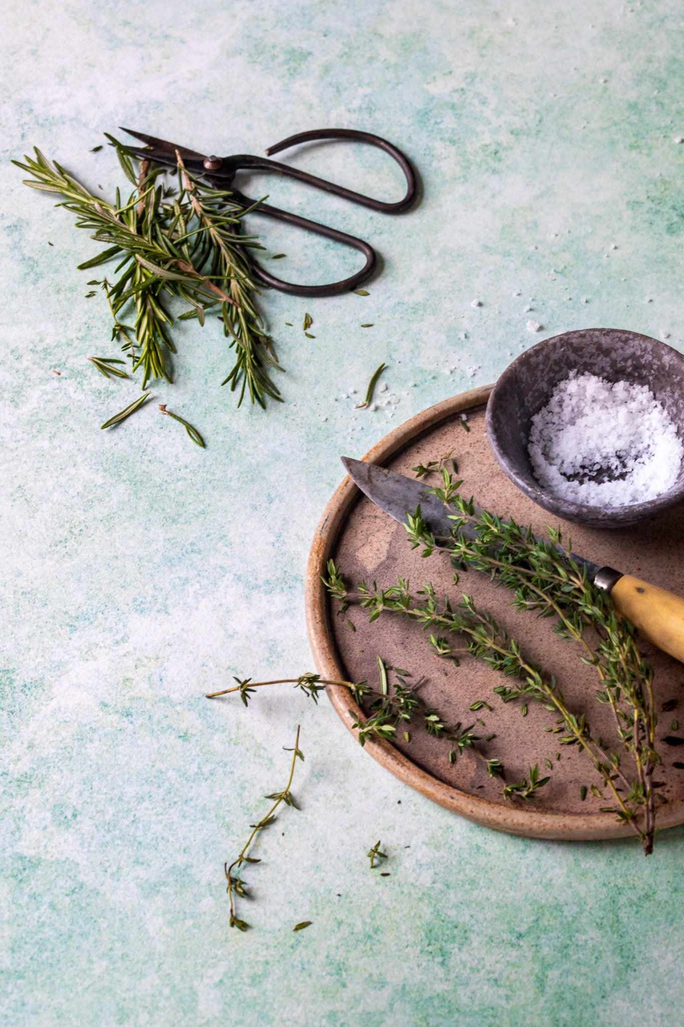 Fresh thyme and rosemary styled on a green mottled marble-effect photography backdrop with shades ranging from soft sage to mint green