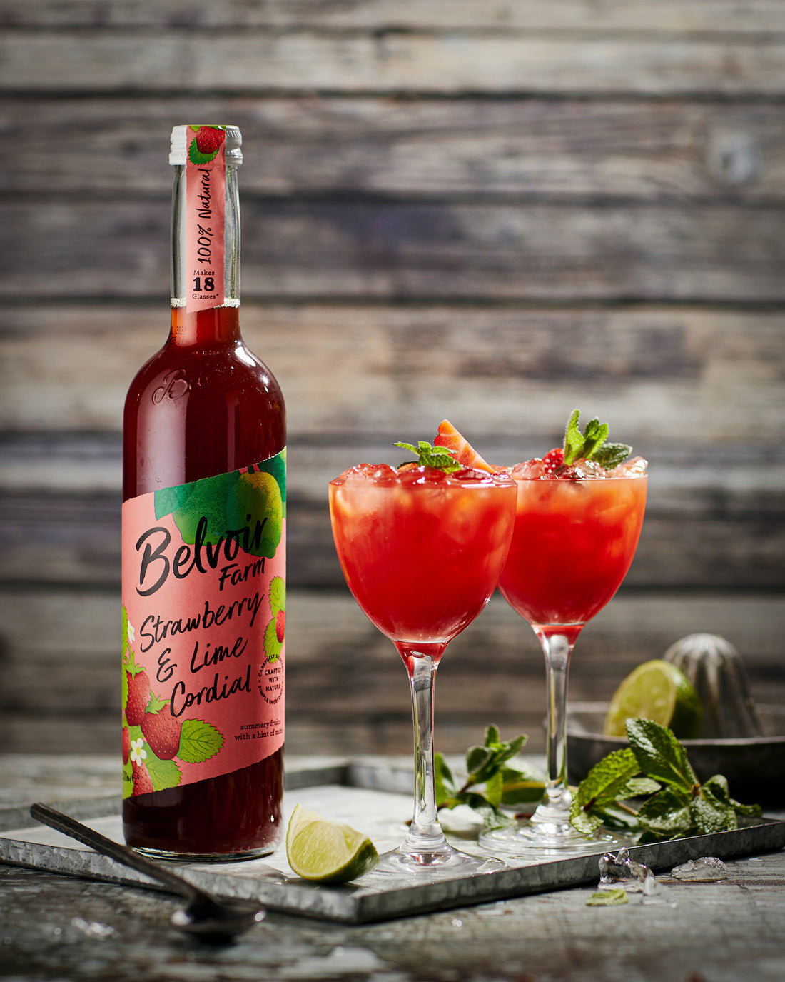 Styled image of Belvoir Farm Strawberry and Lime Cordial shot against a wooden plank-effect vinyl photography backdrop.