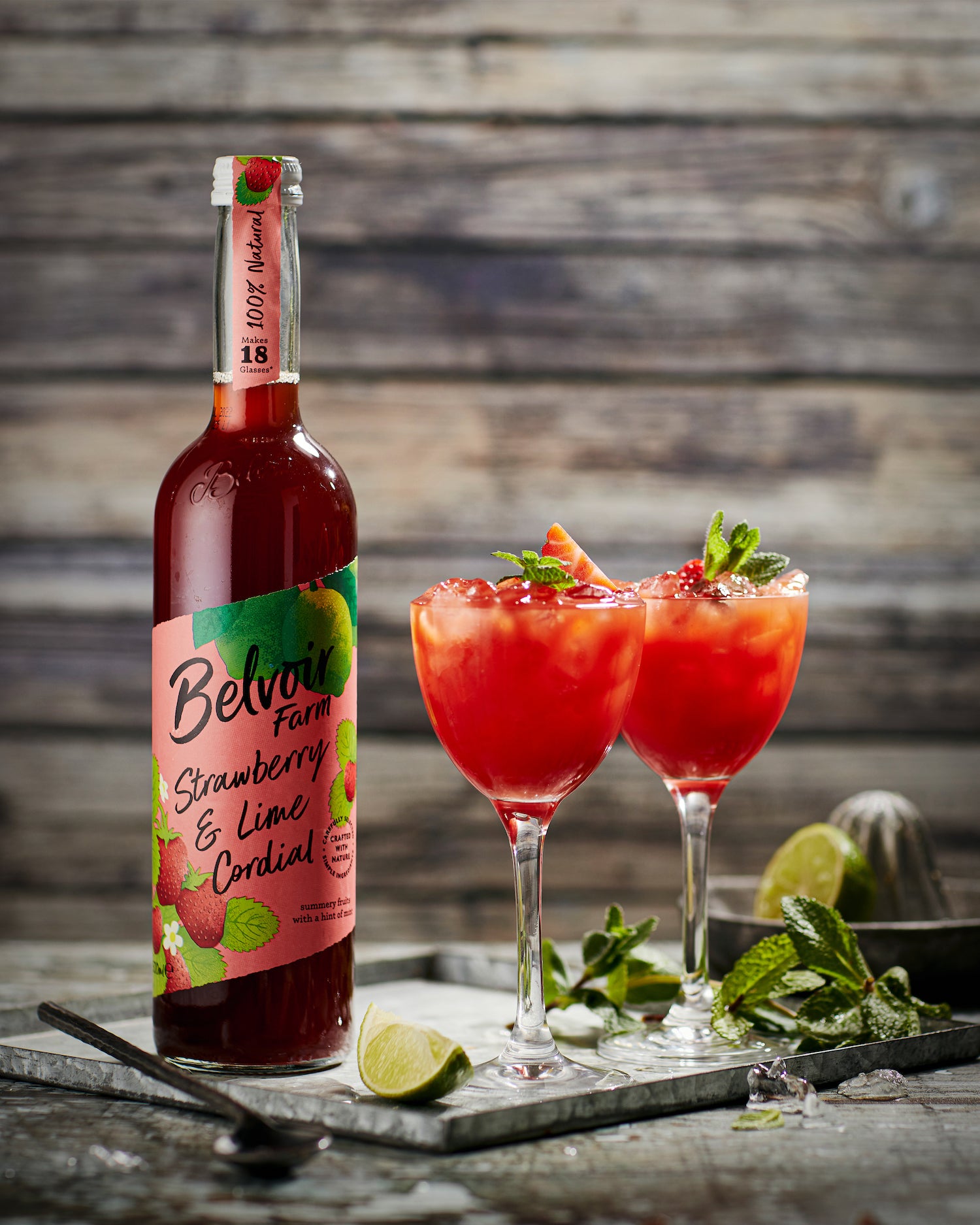 Styled image of Belvoir Farm Strawberry and Lime Cordial shot against a wooden plank-effect vinyl photography backdrop.