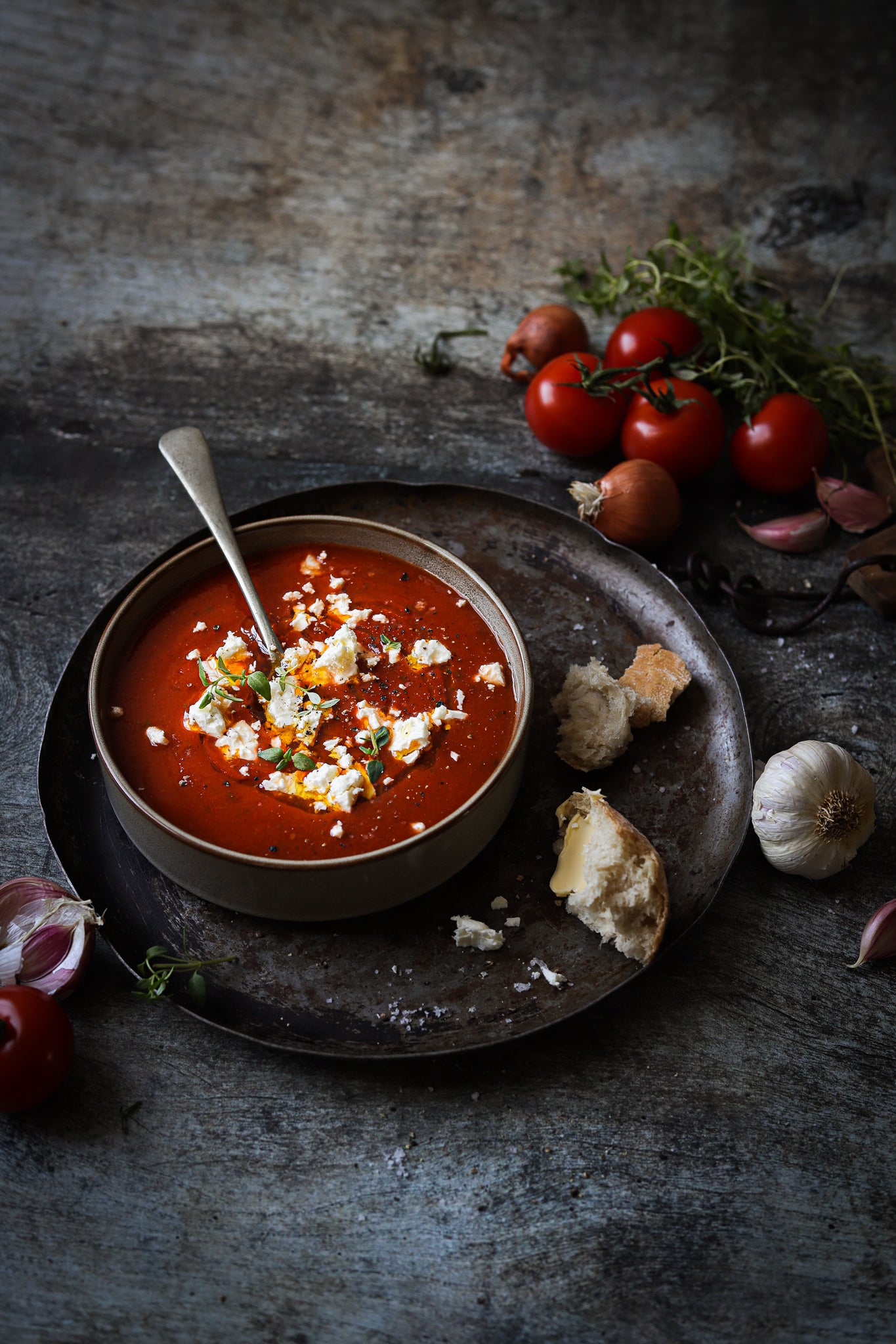 Bowl of homemade tomato soup styled on a rustic photography backdrop with an old wood brown and grey colour palette, suitable for food and product styling.
