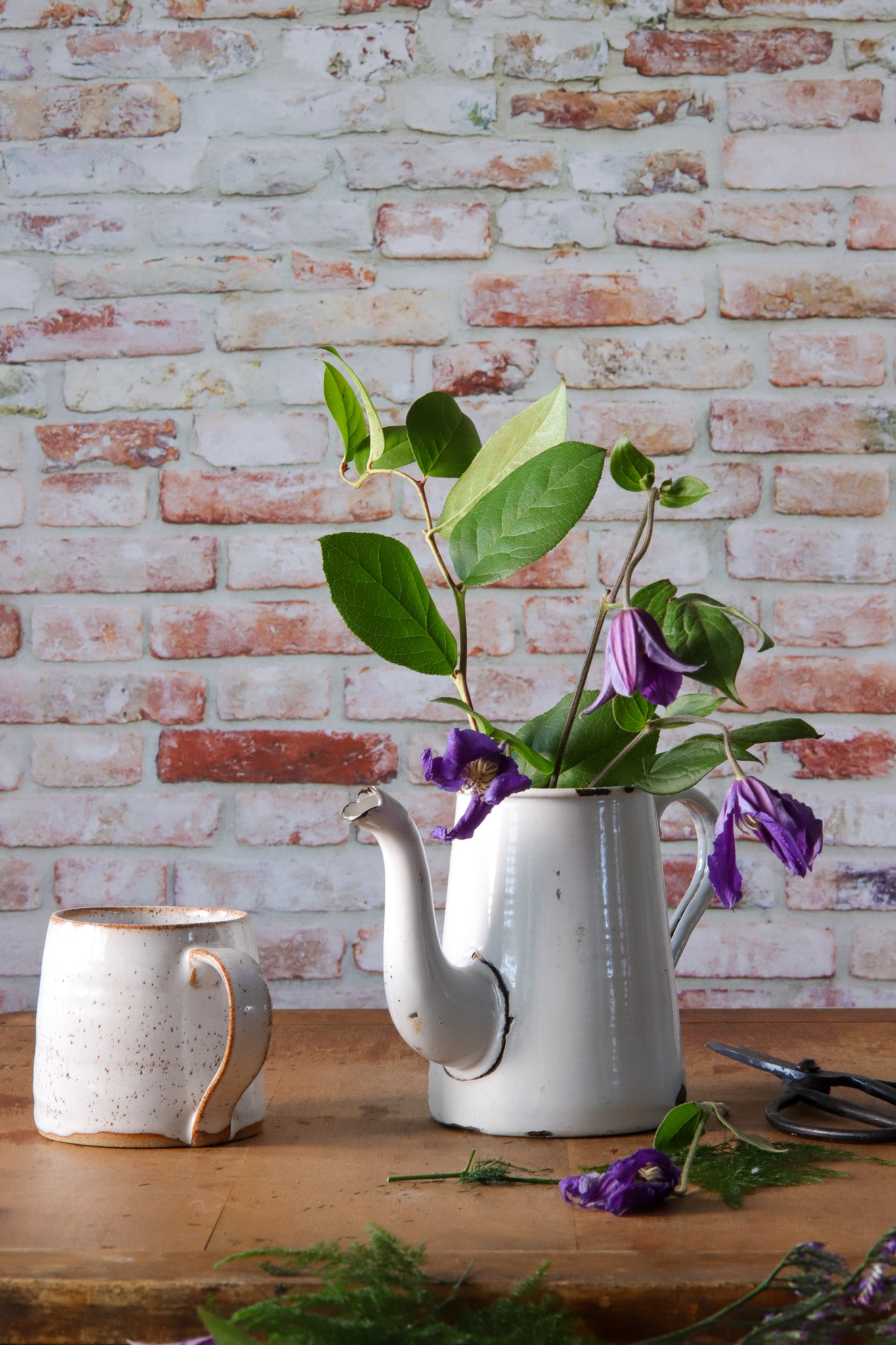 Vintage jug with purple flowers styled against a photography backdrop in a mix of red, grey, and white colors, simulating a rough brick wall texture.