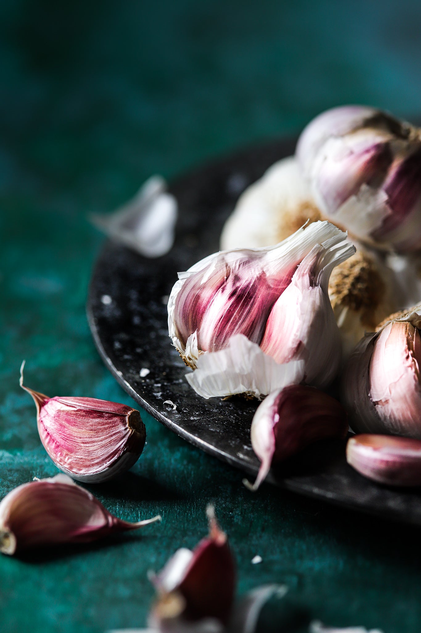 A vintage plate of fresh garlic bulbs styled on a vibrant green vinyl photography backdrop with flaky paint-effect texture.