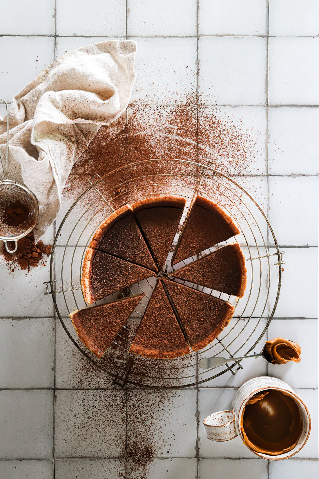 Overhead shot of a dark chocolate flan styled on a white tile effect photography backdrop with a subtle gray grid lines texture.